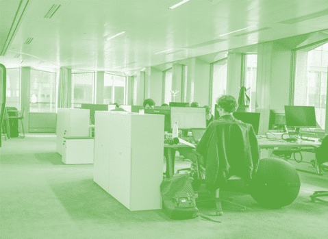 Photo monochrome verte illustrant un espace de travail avec des bureaux et un collaborateur en train de travailler devant son écran d'ordinateur.